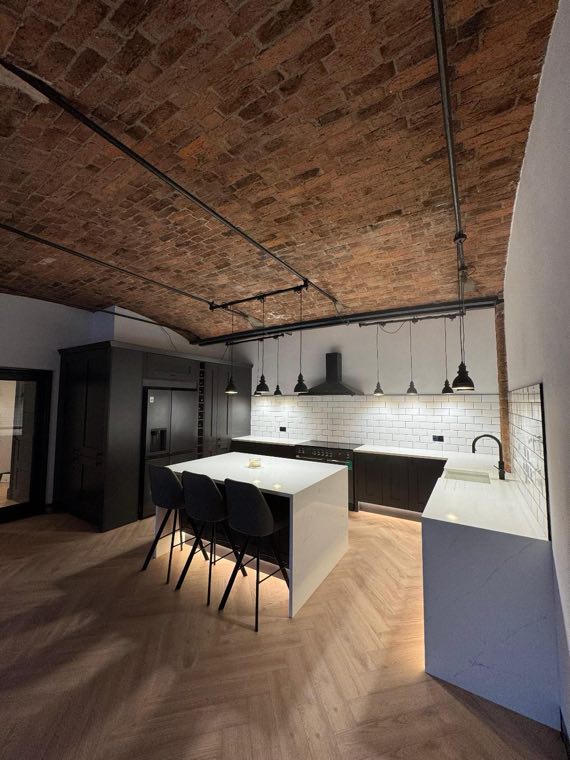 Finished dark kitchen with island under a brick vaulted ceiling
