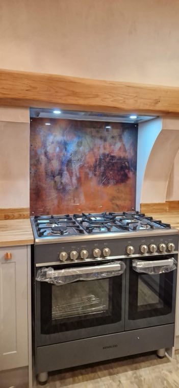 Copper splashback behind a range cooker with a bespoke oak canopy